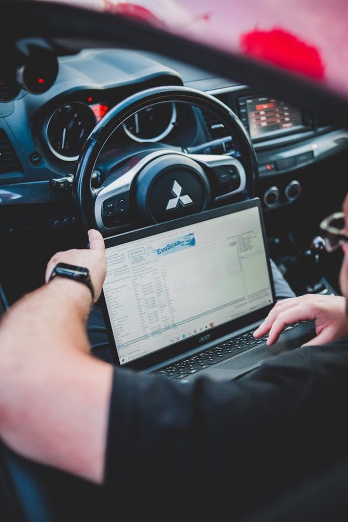 a-man-using-a-laptop-while-sitting-in-a-car-13083209 A person using a laptop inside a car for vehicle diagnostics, showcasing technology integration in automotive settings.